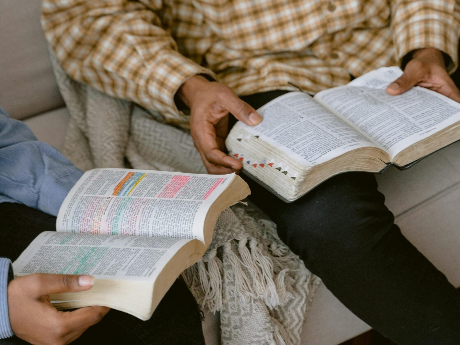 Two individuals sitting on a sofa reading and discussing the Bible indoors.